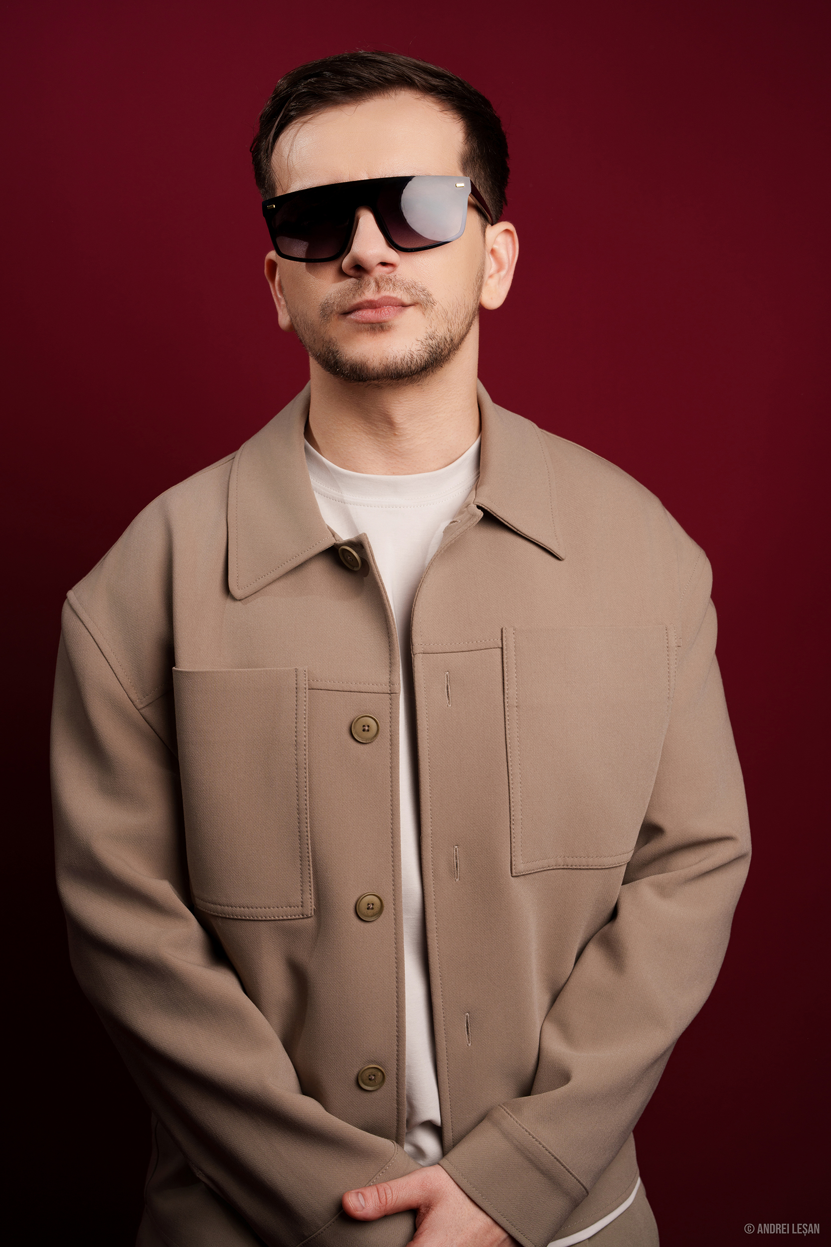 DEEPSYSTEM in a tan jacket and sunglasses against a red studio background